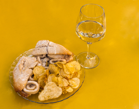 A photo of a squid sandwich, traditional Madrid snack, with a glass of white wine, on a vibrant yellow background, with copyspaceの写真素材