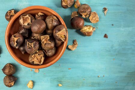 A photo of peeled and unpeeled roasted chestnuts in an earthenware bowl, shot from above on a vibrant blue background with copyspaceの写真素材