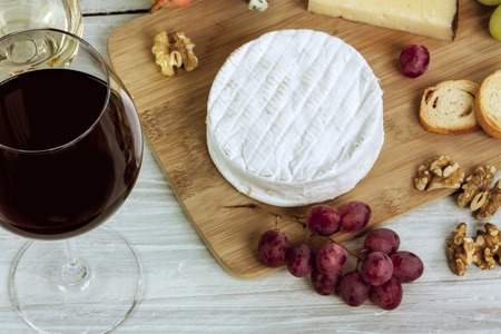 A photo of a tasting with glasses of wine, cheese, nuts, and grapes, on a wooden boardの写真素材