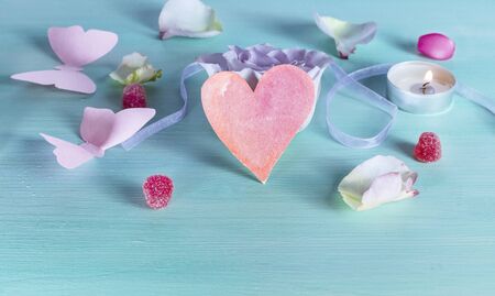 A Valentine day card with a rose flower, a paper butterfly, sweets, candles, a little cutout heart, and copyspace, slightly tonedの写真素材