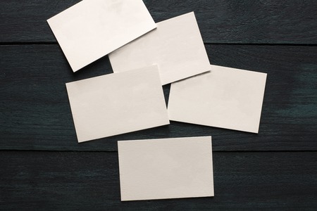 A photo of blank white thick cardboard business cards on a dark wooden background texture. A mockup or a minimalist banner with copyspaceの写真素材