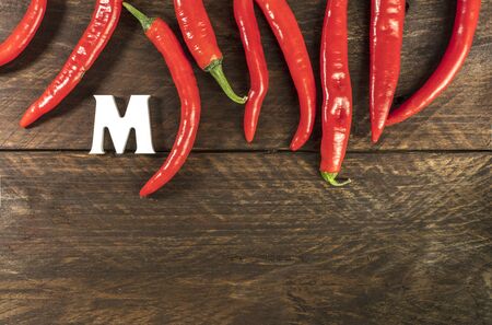 Red hot chili peppers, shot from above on a dark brown wooden texture, with the letter M for Mexico and copyspaceの写真素材