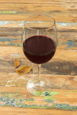 A photo of a glass of red wine with autumn leaves, shot on a blurred wooden boards background texture with copy space. Selective focusの写真素材