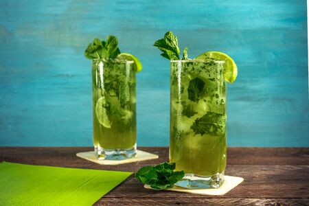 A photo of mojito cocktails with mint leaves and wedges of lime, on a vibrant teal wooden background with copy space. Selective focusの写真素材