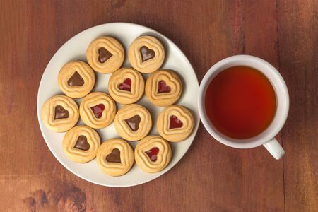 A cup of tea with many little cookies with chocolate and jam filling, shot from above on a dark wooden background with copyspaceの写真素材