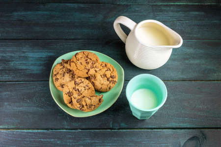 A plate of chocolate chips cookies on a dark blue background, with a glass and jar of milk and copy spaceの写真素材