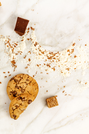 The process of making chocolate chips cookies. Overhead shot of biscuits with grated chocolate, cane sugar, flour, and copy spaceの写真素材