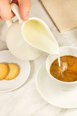 A photo of milk being poured into a cup of coffee. Selective focus, toned imageの写真素材