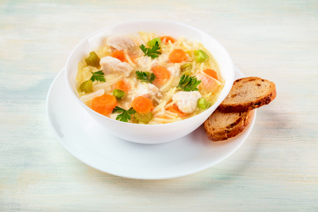 Chicken soup with noodles and bread on a light backgroundの写真素材