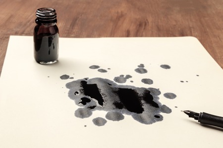 A photo of drops of ink on paper, an ink well and and a nib pen, with copy spaceの写真素材