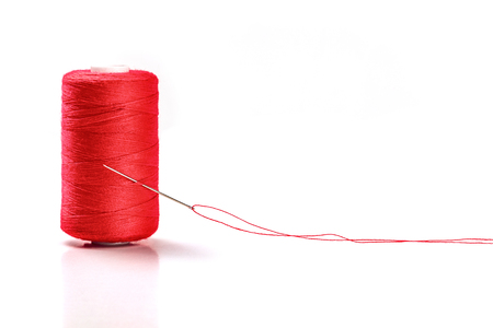 A photo of a needle with a red thread and a spool on a white backgroundの写真素材