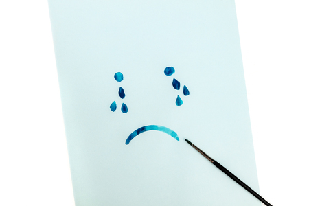 Blue, sad face with tears, hand painted on blue paper in watercolor, depression concept, with copy spaceの写真素材