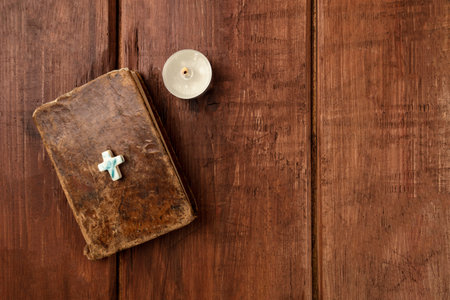 Old bible with a cross and a candle on a dark background with copy space