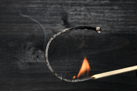 A side view of a burning match, with fire and smoke, on a dark background with copy spaceの写真素材