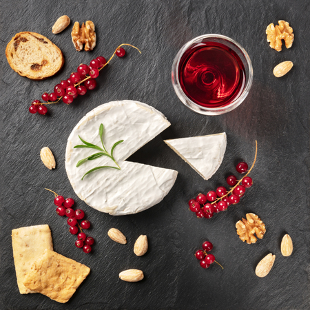 An overhead photo of Camembert cheese with a glass of red wine, fruits and nuts, shot from above on a black background with copy spaceの写真素材