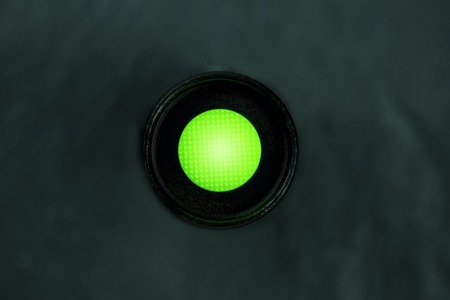 An overhead photo of a vibrant green button on a dark panel with copy spaceの写真素材