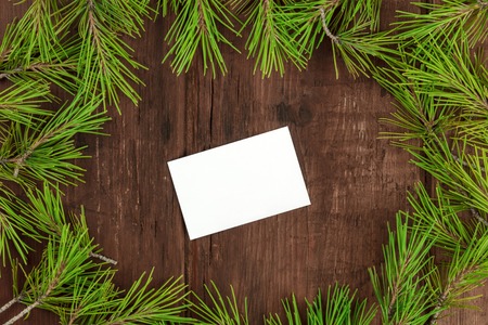 A Christmas frame with fir tree branches on a dark wooden background, with a blank business card with copy space, shot from the topの写真素材