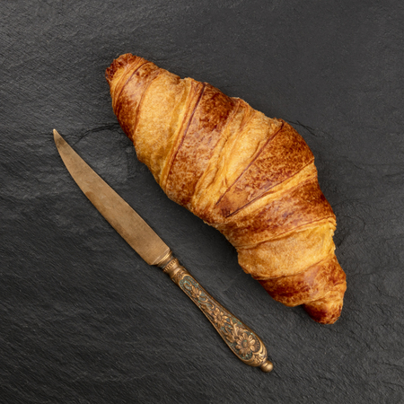 An overhead photo of a croissant with a vintage knife, shot from the top on a black background with copy spaceの写真素材