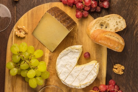 An overhead photo of cheeses, Camembert and a cured cheese, with grapes and nuts on a dark rustic wooden backgroundの写真素材