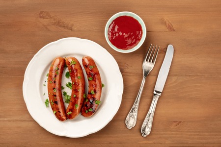 A photo of a plate of fried sausages with ketchup, shot from the top on a dark rustic wooden background with a place for textの写真素材