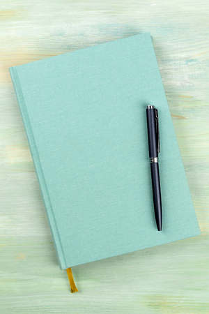 A blue journal with a pen, an elegant diary, notebook or planner, shot from the top on a teal green backgroundの写真素材