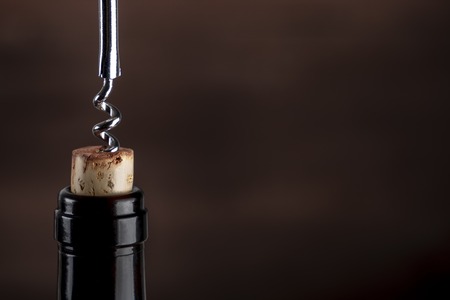 A closeup photo of a corkscrew pulling a cork from a bottle of wine on a dark background with copy spaceの写真素材