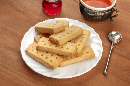 A photo of Scottish shortbreads, typical British butter cookies, on a rustic background with a vintage cup of tea, jam, and a place for textの写真素材