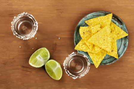 A photo of two tequila shots with lime slices and nachos, Mexican chips, shot from the top on a dark rustic background with copy spaceの写真素材