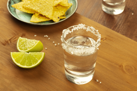 A photo of tequila shots with lime slices and nachos, Mexican chips, on a dark rustic background with copy spaceの写真素材