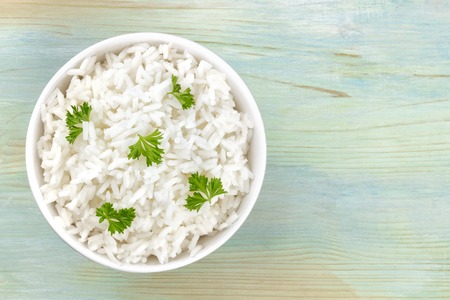 A photo of a bowl of cooked white long rice, shot from the top on a teal blue background with copy spaceの写真素材
