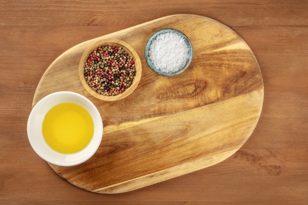 A cutting board, shot from the top on a dark rustic texture with salt, pepper, olive oil, and a place for text. A cooking background with copy spaceの写真素材