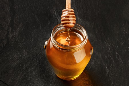 A photo of a bamboo honey dipper and a jar of organic honey on black background with a place for textの写真素材
