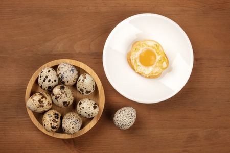 A photo of quail eggs, shot from the top on a dark rustic wooden background with an egg cooked sunny side up and a place for textの写真素材