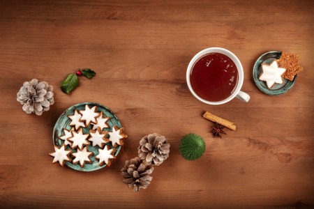 A photo of Zimsterne, traditional German cinnamon star cookies, shot from the top on a dark rustic background with hot chocolate, spices, a toy Christmas tree, pine cones, and a place for textの写真素材