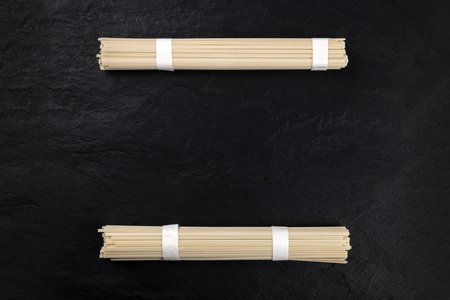 Two individually wrapped portions of udon noodles, shot from the top, forming a frame on a black background with copy spaceの写真素材
