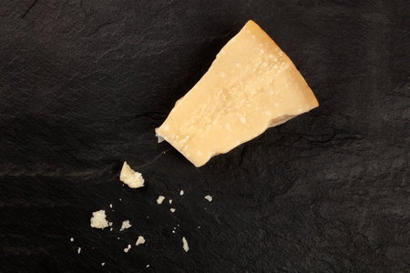 A piece of aged Parmesan cheese with crumbs, shot from the top on a black background with a place...