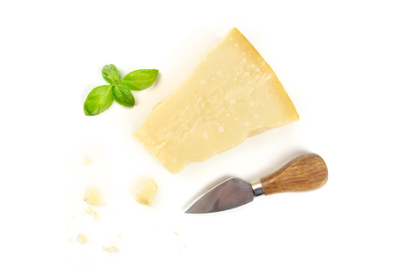 A piece of aged Parmesan cheese with crumbs, shot from the top on a white background with fresh basil leaves, a cheese knife, and copy spaceの写真素材