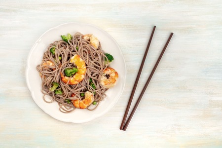 An overhead photo of soba, buckwheat noodles, with shrimps and vegetables, shot from above with chopsticks on a pale wooden backgroundの写真素材