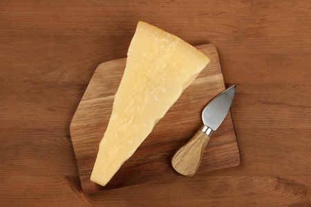 A piece of aged Parmesan cheese with a knife, shot from above on a dark rustic wooden background with a place for textの写真素材