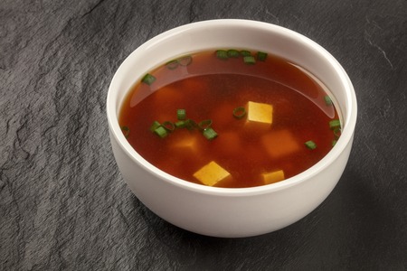 A bowl of miso soup with tofu and scallions on a black background with a place for textの写真素材