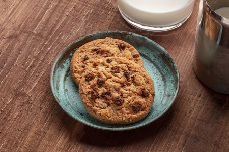 A closeup photo of chocolate chip cookies with milk on a dark rustic wooden background with copy spaceの写真素材