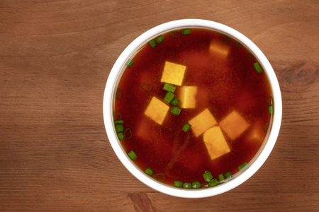 A bowl of miso shiru soup with tofu and scallions, shot from above on a dark rustic background with a place for textの写真素材