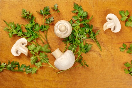 Champignons, whole and sliced, shot from the top on a rustic cutting board with fresh parsley leaves and a place for textの写真素材