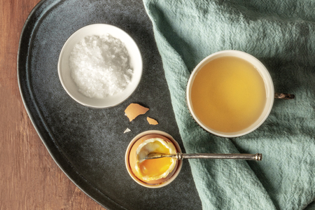 A soft-boiled egg with coarse sea salt and tea, shot from above on a dark rustic wooden backgroundの写真素材