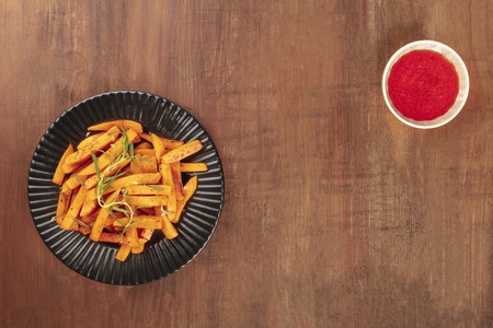 Roasted sweet potato fries with rosemary and ketchup, shot from above on a dark rustic wooden background, forming a frame with a place for textの写真素材