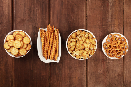 Salty crackers, sticks, pretzels, and goldfishes, shot from the top on a dark wooden background with copy space. Party snacks mix with a place for textの写真素材