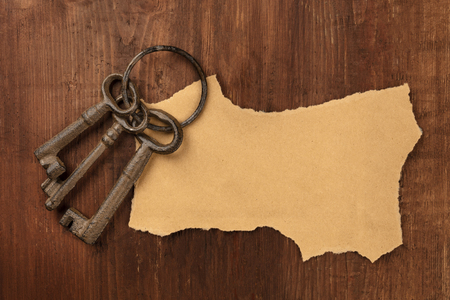 A piece of torn brown craft paper, shot from the top on a dark wooden background with old keys on a ring and a place for textの写真素材