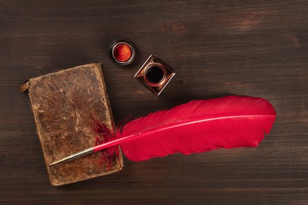 An ink well with an old journal and a vibrant quill pen, shot from the top on a dark wooden background with a place for textの写真素材