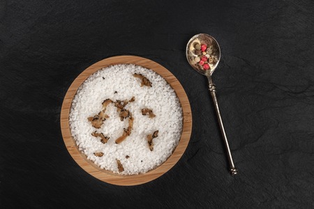 Gourmet spices. A bowl of sea salt infused with truffle shavings and a pepper mix, shot from above on a black background with a place for textの写真素材
