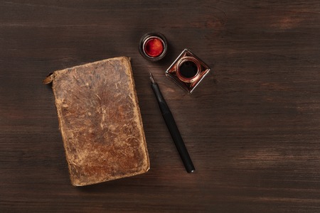 An old journal with a nib pen and an ink well, shot from the top on a dark wooden background with a place for textの写真素材